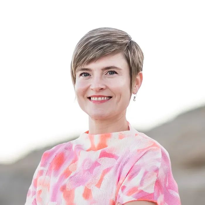 Maria "Masha" Steiner-Renoir, PMHNP-BC, smiling in a pink and coral patterned top, short light brown hair, outdoors