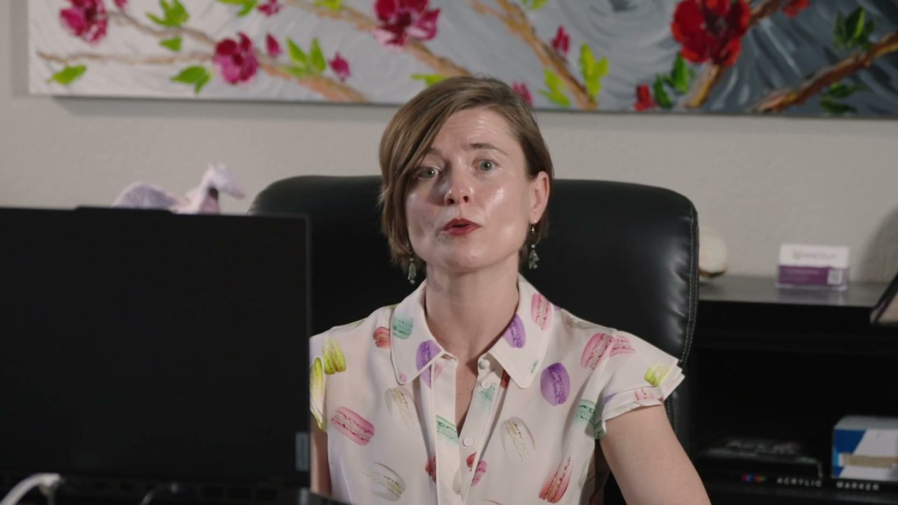 Masha Steiner-Renoir at her office desk, a painting of pink and red blossoms on the wall behind her