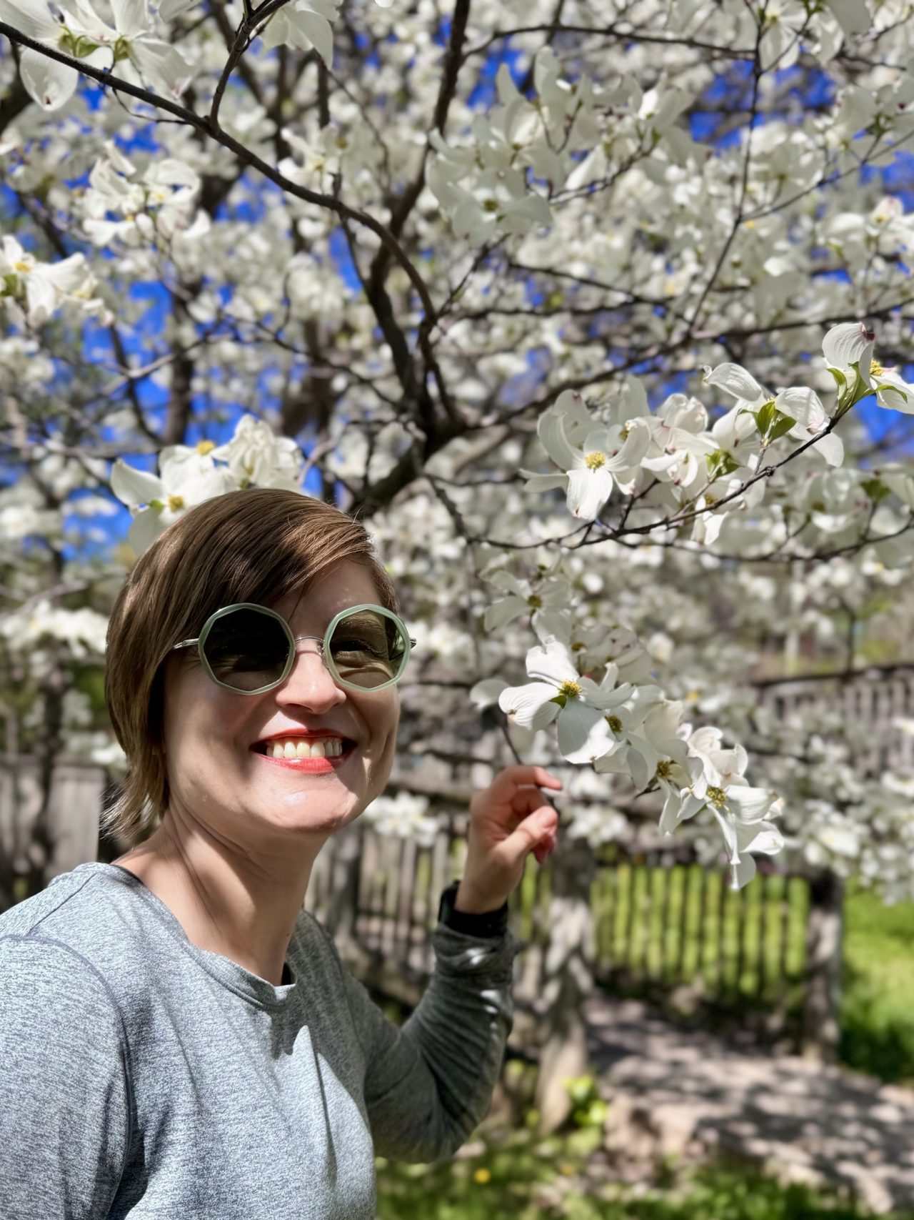 Masha in sunglasses smiling under a tree in full white blossom