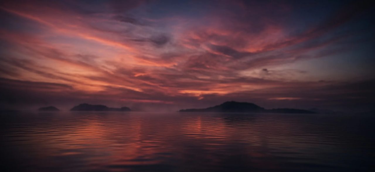 Pink and purple clouds at dusk reflected in still water, low islands on the horizon