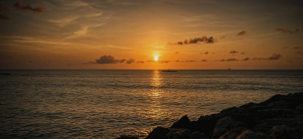 The sun setting over the ocean, its light on the water, rocks in the foreground