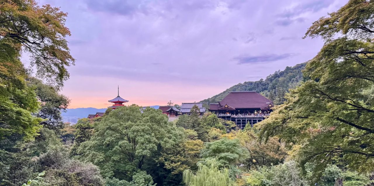 A pagoda and temple roofs rising from wooded hills at dusk under a lavender sky