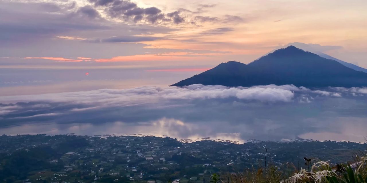 A volcano above a sea of clouds at sunrise, with a lakeside town in the valley below